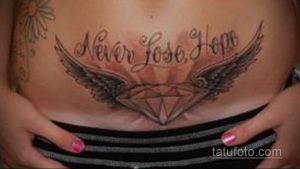 Фото тату надписи "Never Lose Hope" с изображением бриллианта и крыльев на женском животе. Элегантный рисунок в черно-серых тонах.