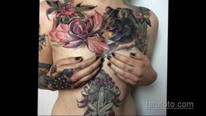 Фото тату с изображением медведя, окруженного цветами на женской груди. Детализированный рисунок с использованием ярких цветов и мягких переходов.