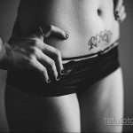 Крупный план женского живота с татуировкой надписью 'REBORN'. Черно-белое фото, акцентирующее внимание на детализации шрифта и расположении татуировки.