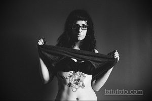 Фотография девушки с татуировкой на животе в виде черепа, обвитого розами. Черно-белое изображение, демонстрирующее детализированный рисунок татуировки.