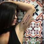 Фото тату с изображением двух минималистичных стрел на подмышечной впадине. Черные линии, тонкая проработка, современный стиль.