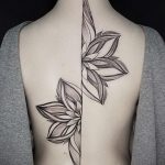 Фото тату: симметричный рисунок цветка, разделенный пополам на спине. Черно-белая татуировка в стиле графика.