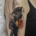 Фото тату: реалистичное изображение ворона с цветущей сакурой на плече. Красивый и символичный рисунок татуировки в японском стиле.
