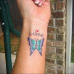 Фото тату: яркая бабочка с надписью 'believe' на запястье. Рисунок татуировки выполнен в акварельном стиле с использованием синих, фиолетовых и розовых оттенков.