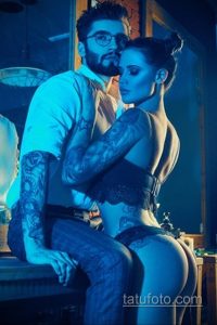 Фото тату на теле пары. Татуировки в основном на руках и плечах, выполнены в реалистичном стиле. Пара обнимается в полумраке.