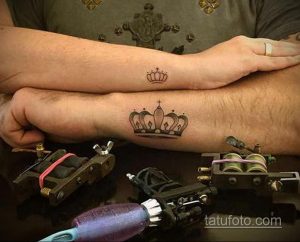 Фото татуировок на руке: большая черная корона на предплечье и маленькая корона на запястье.
