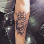 Фото татуировки льва с короной на предплечье. Черно-серая татуировка в реалистичном стиле, изображающая рычащего льва.