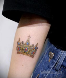 Фото тату: яркая, детальная корона с драгоценными камнями на женском предплечье. Идеальный эскиз тату для ценителей королевского стиля.
