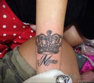 Фото тату на запястье: татуировка короны над именем 'Momo', выполненная в черно-серых тонах. Индивидуальный рисунок татуировки.