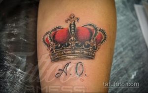 Фото тату: корона с инициалами "A.O." на руке, красный камень в короне, классический стиль, детализированный рисунок.
