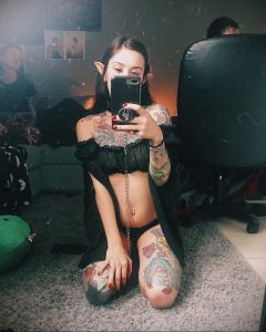Фотография девушки с эльфийскими ушами и татуировками на теле, демонстрирующей свой образ в зеркале. Изображение создает атмосферу загадочности и волшебства.