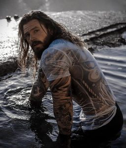 Фотография мужчины с татуировками на теле, стоящего в воде. Идеально для поиска идей для тату в стиле акварель и органические узоры.