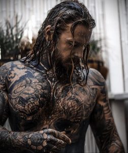 Фотография мужчины с татуировками на теле, стоящего под струями воды. Идеально для поиска идей для тату в стиле блэкворк и геометрия.