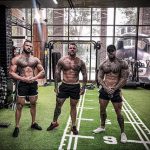 Фотография трех спортивных мужчин с обширными татуировками на теле, позирующих в современном тренажерном зале. Идеально для поиска идей для тату и вдохновения.