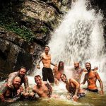 Группа друзей с татуировками весело проводит время у водопада. Фотография демонстрирует любовь к приключениям и боди-арту.