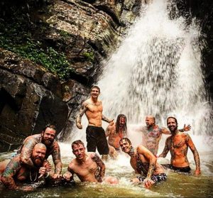 Группа друзей с татуировками весело проводит время у водопада. Фотография демонстрирует любовь к приключениям и боди-арту.