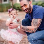 Фотография мужчины с татуировками на руках, обнимающего маленькую девочку, испачканную кремом. Изображение передает тепло и семейную любовь.