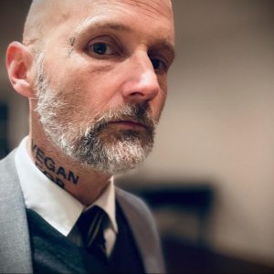 Фото тату надписи 'VEGAN FOR LIFE' на шее мужчины. Черная татуировка, выполненная простым шрифтом, подчеркивает жизненную позицию владельца.