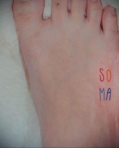 Фото тату: надпись 'SO MA' выгравирована на верхней части стопы, используя красный и синий цвета чернил. Минималистичный стиль.