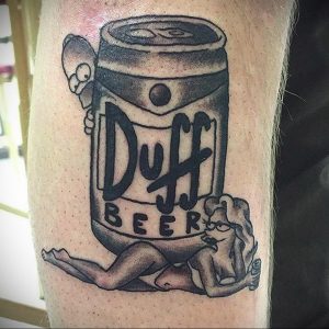 Фото тату на ноге с изображением банки пива Duff Beer из "Симпсонов" и девушки в стиле пин-ап. Черно-белый эскиз в традиционном стиле.