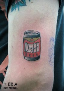 Фото татуировки на руке с изображением банки пива Duff Beer из мультсериала Симпсоны. Простой и узнаваемый рисунок татуировки в ярких цветах.