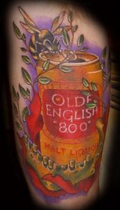 Фото татуировки на руке с изображением банки пива Olde English, пчелы и черепа. Детализированный рисунок татуировки в ярких цветах и необычной композиции.