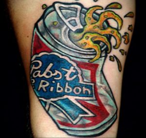 Фото татуировки на руке с изображением открывающейся банки пива Pabst Blue Ribbon, из которой выплескивается пиво. Динамичный рисунок татуировки в ярких цветах.