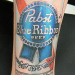 Фото большой татуировки на руке с изображением банки пива Pabst Blue Ribbon. Детализированный рисунок татуировки с реалистичными элементами и надписями.
