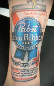 Фото большой татуировки на руке с изображением банки пива Pabst Blue Ribbon. Детализированный рисунок татуировки с реалистичными элементами и надписями.