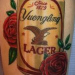 Фото тату: татуировка на руке с банкой пива Yuengling, украшенной розами и логотипом бренда.