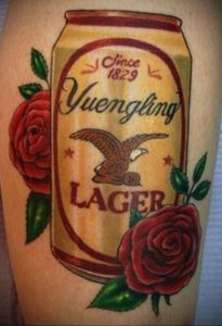 Фото тату: татуировка на руке с банкой пива Yuengling, украшенной розами и логотипом бренда.