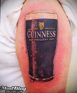 Фото тату: реалистичное изображение кружки пива Guinness с логотипом и пузырьками на плече.