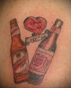 Фото тату на спине с изображением двух бутылок пива и сердца с надписью "Love at 1st Sip". Оригинальный и символичный рисунок татуировки.