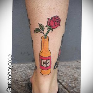 Фото тату на ноге с изображением бутылки пива Duff Beer из мультсериала Симпсоны. Яркий и запоминающийся рисунок татуировки в стиле мульт.