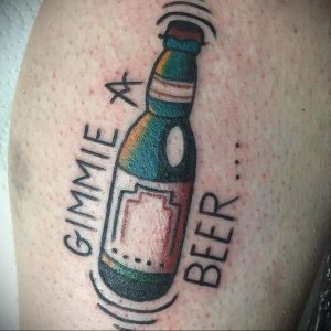 Фото тату на руке с изображением бутылки пива и надписью "Gimmie a Beer". Простой и дерзкий рисунок татуировки в стиле олдскул.