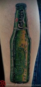 Фото тату на руке с изображением бутылки пива Carlsberg. Детализированный и реалистичный рисунок татуировки в зеленых тонах.