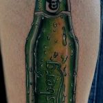 Фото тату на руке с изображением бутылки пива Carlsberg. Детализированный и реалистичный рисунок татуировки в зеленых тонах.