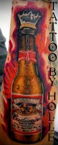 Фото тату на руке с изображением бутылки пива Budweiser, украшенной короной. Яркий и красочный рисунок татуировки в стиле реализм.