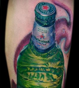Фото тату на руке с изображением бутылки пива Heineken и клубов дыма. Яркий и динамичный рисунок в зеленых и фиолетовых тонах.