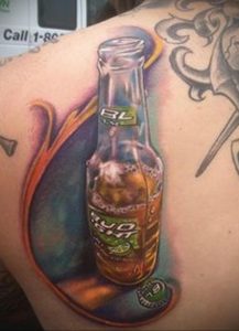Фото тату на плече с изображением бутылки пива BL Lager. Реалистичный рисунок с использованием коричневых, желтых и оранжевых оттенков.