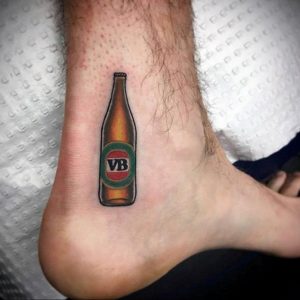 Фото тату на лодыжке с изображением бутылки пива VB. Простой и лаконичный рисунок в ярких цветах.
