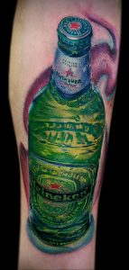 Фото тату на руке с реалистичным изображением бутылки пива Heineken. Детализированный рисунок с использованием зеленых, красных и белых оттенков.