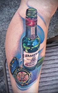 Фото тату: реалистичная татуировка бутылки виски Jameson и старинного компаса на руке. Детализированный рисунок татуировки.