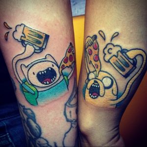 Фото тату персонажей мультсериала Adventure Time Финна и Джейка с пивом и пиццей на предплечьях. Яркий рисунок татуировки в мультяшном стиле.