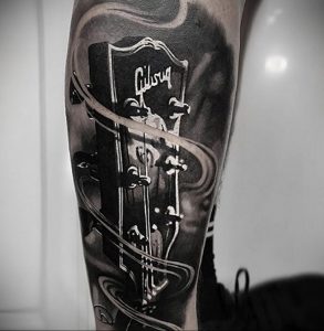 Фото тату на руке: реалистичная черно-белая татуировка гитары Gibson с динамичными линиями и тенями. Детализированный рисунок татуировки.