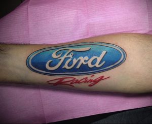Фото тату: логотип Ford Racing на руке, яркие цвета, синий и красный, татуировка для поклонников автомобилей Ford.
