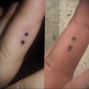Фотография минималистичной татуировки с изображением двух точек с запятой на пальце, символизирующей поддержку и надежду.