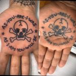 Фотография минималистичной татуировки на ладони с изображением черепа и костей, окруженного фразой "As you are, I was, as I am, you will be".