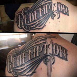 Фото татуировки на спине с надписью 'REDEMPTION', выполненной в каллиграфическом стиле. Черно-белый рисунок, декоративные элементы.
