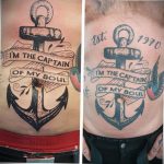 Фото тату на спине с изображением якоря, веревки и надписи 'I'M THE CAPTAIN OF MY SOUL' в традиционном морском стиле. Яркий рисунок татуировки.